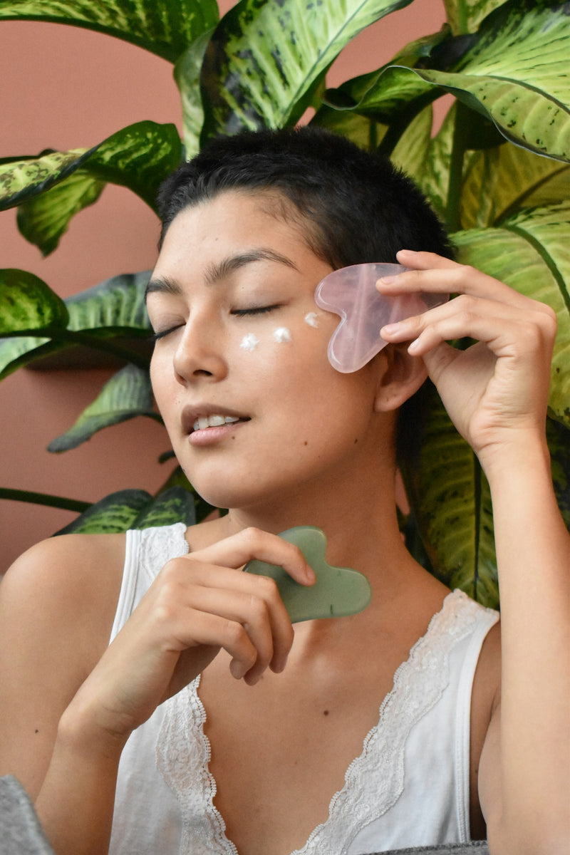 Femme utilisant un gua sha en quartz rose sur le visage et en jade sur le cou