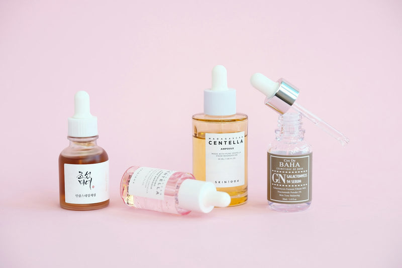 Plusieurs sérums et flacons compte-gouttes d'actifs cosmétiques disposés ensemble, illustrant l'association des actifs
