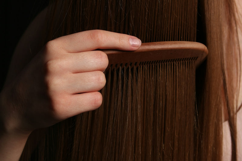 Main passant dans une longue chevelure brune, illustrant la chute de cheveux chez la femme